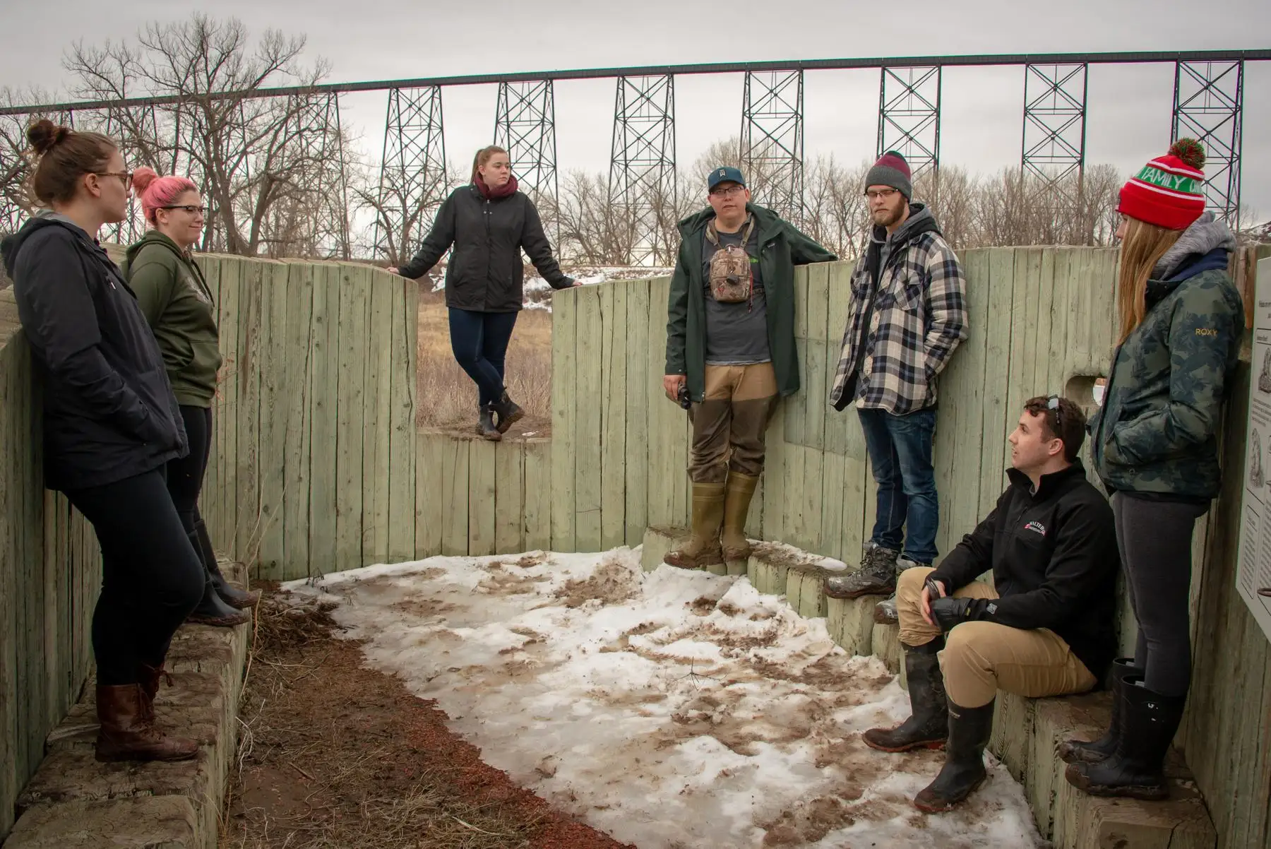 A group of people standing inside a wooden wildlife blind in winter