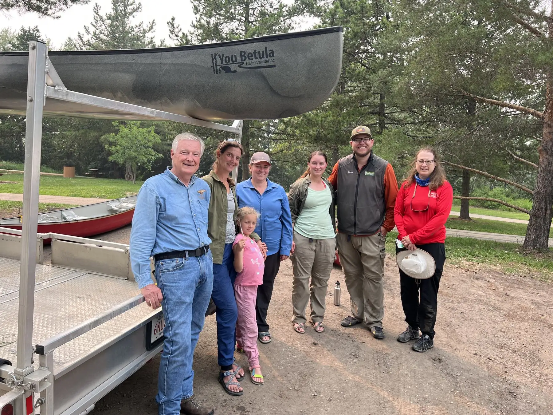 A group of people standing in front of a trailer loaded with You Betula canoes