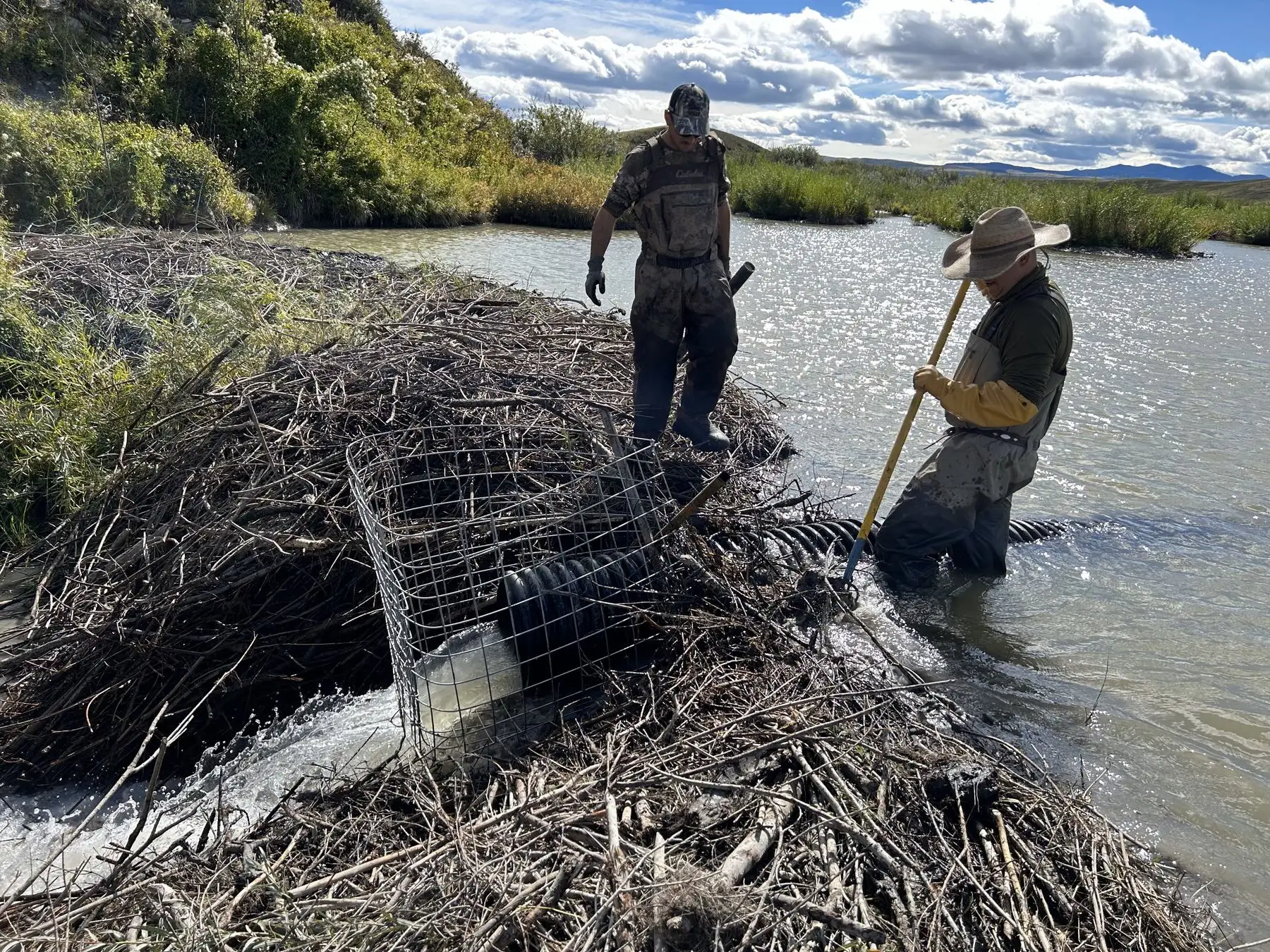 Two people finishing a pond leveller install at Morkin Farms, standing in the pond beside the caged intake