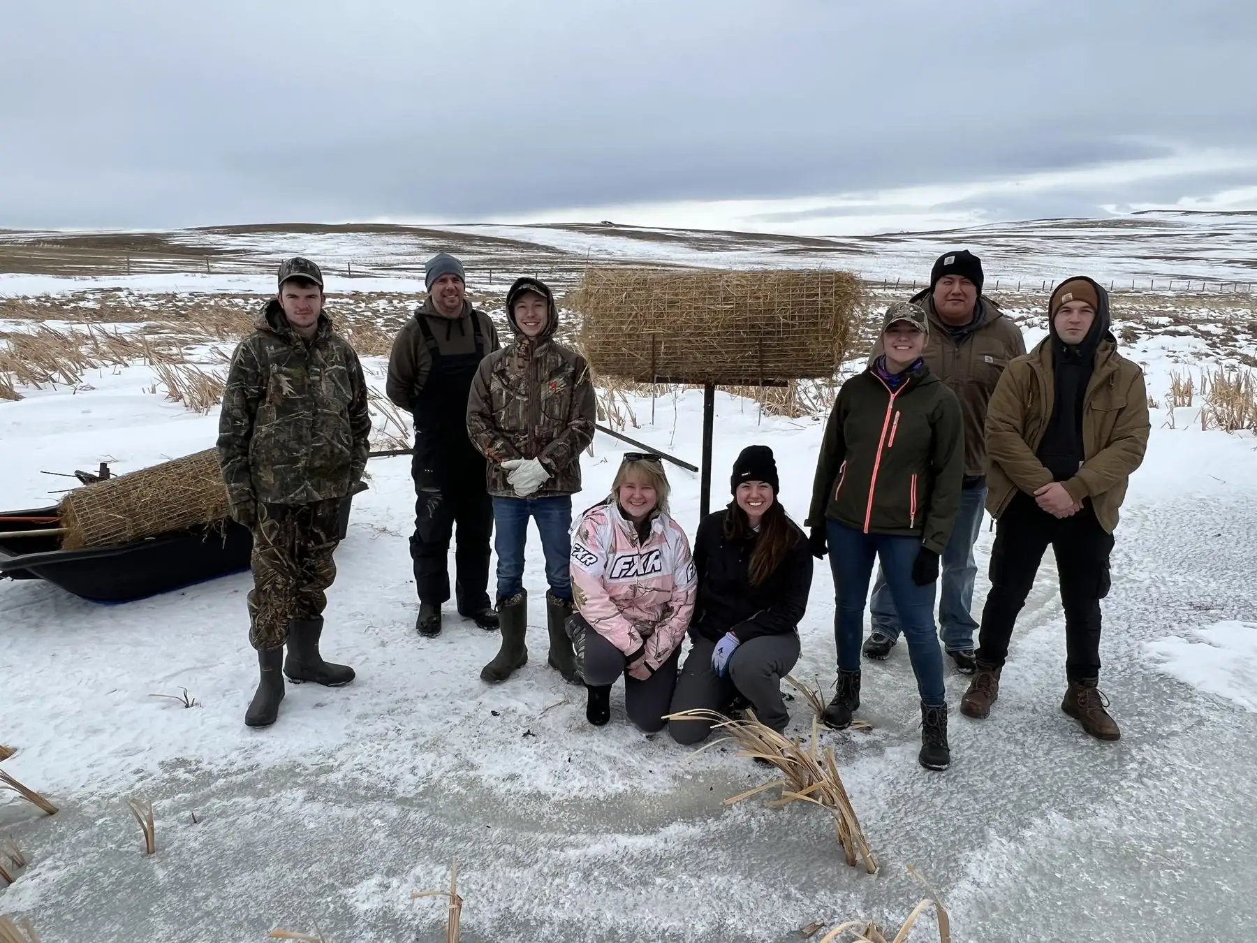 A work crew posing in the snow in front of a straw structure
