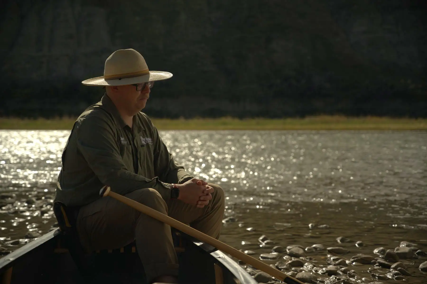 Kirby England in a canoe at the edge of the river, backlit by low sun