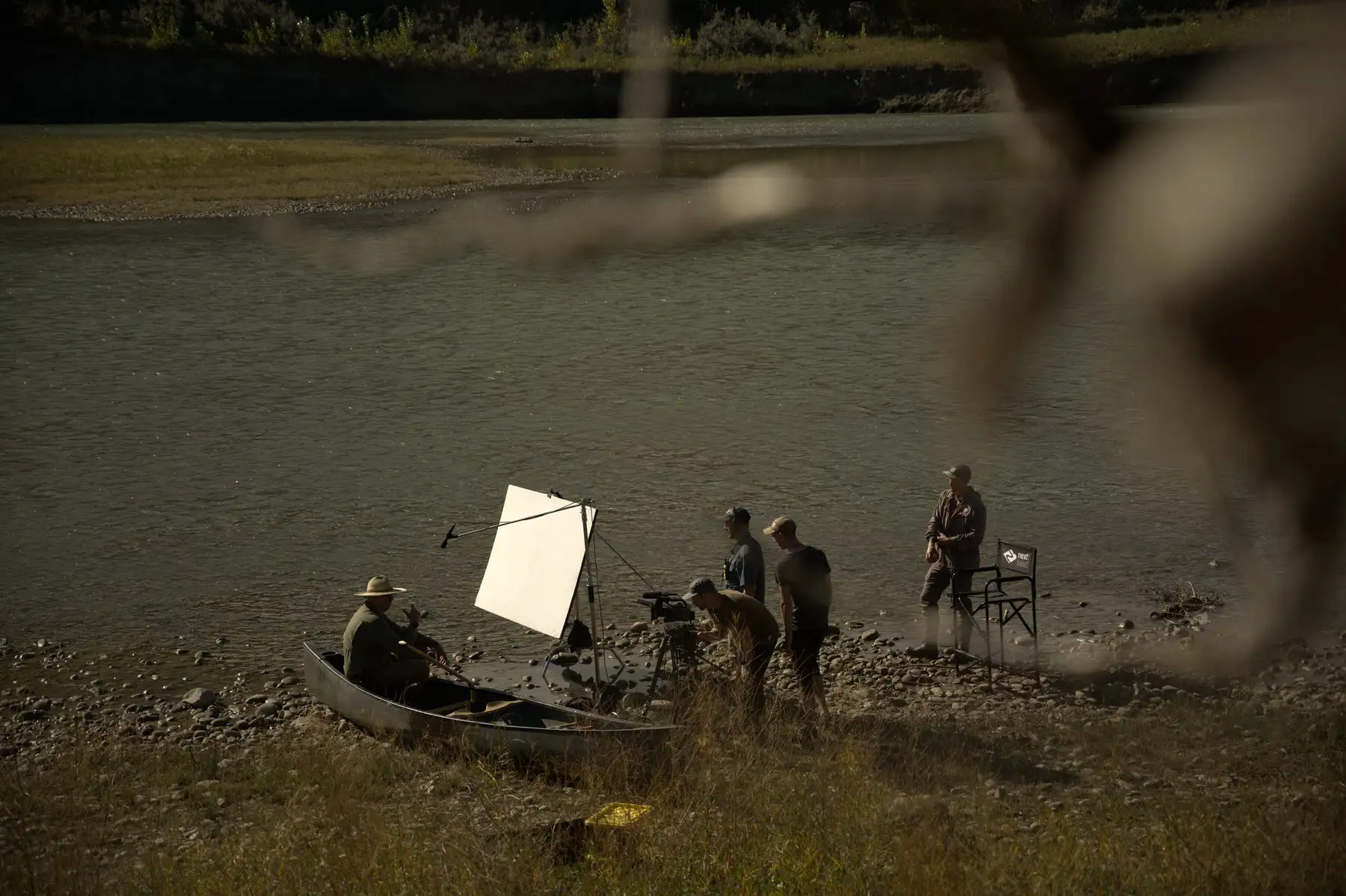 A film crew on a gravel bar of the Oldman River, filming Kirby in a canoe